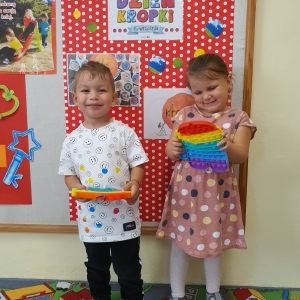 Kropeczkowa moda” dwoje dzieci w ubrankach w kropki stoi i bawi się kolorowym „Poppitem”.