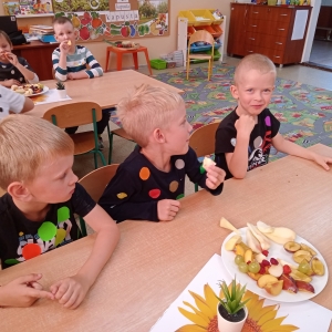 Dzieci siedzą przy stolikach i jedzą owoce