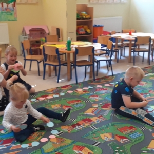 Dzieci siedzą na dywanie i układają z kół wymyślone przez siebie budowle, zwierzęta, rośliny