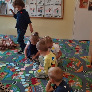 Kilkoro dzieci układa na dywanie dom z papierowych kół, jedno dziecko stoi