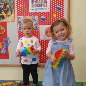 „Kropeczkowa moda” dwoje dzieci w ubrankach w kropki stoi i bawi się kolorowym poppitem