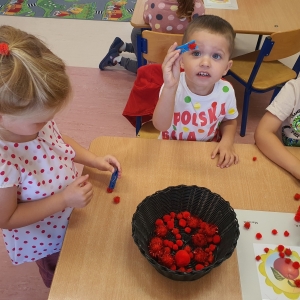 Dzieci za pomocą klamerek przenoszą czerwone pomponiki do koszyczka