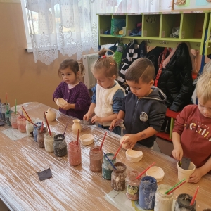 Dzieci przygotowują gliniane naczynia do malowania (przecierają papierem ściernym)