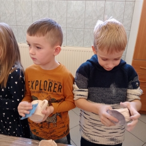 Dzieci przecierają papierem ściernym gliniane naczynia.