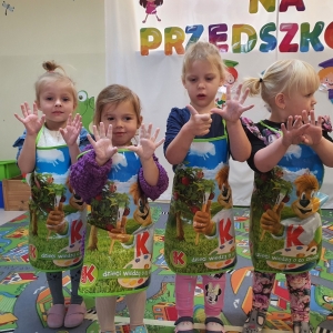 Dzieci ubrane w fartuszki ochronne pokazują swoje ubrudzone od farby rączki.